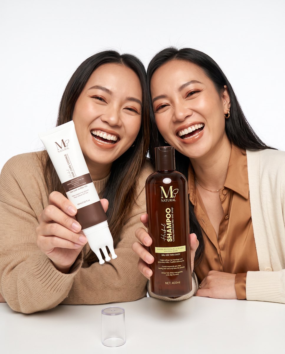 Hai cô gái Việt cười tươi bên bộ sản phẩm chăm sóc tóc M Natural