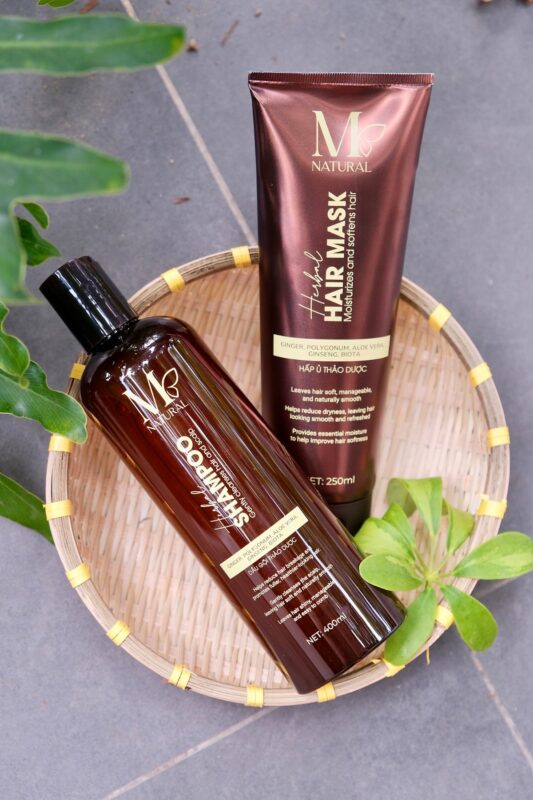 Chai dầu gội và tuýp kem hấp ủ M Natural đặt trên khay gỗ tròn