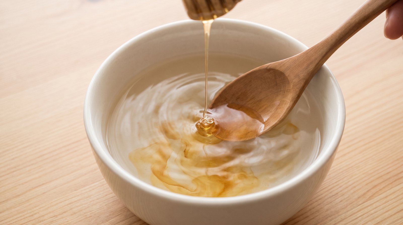 Pha loãng mật ong vào bát nước ấm bằng thìa gỗ trước khi ủ tóc
